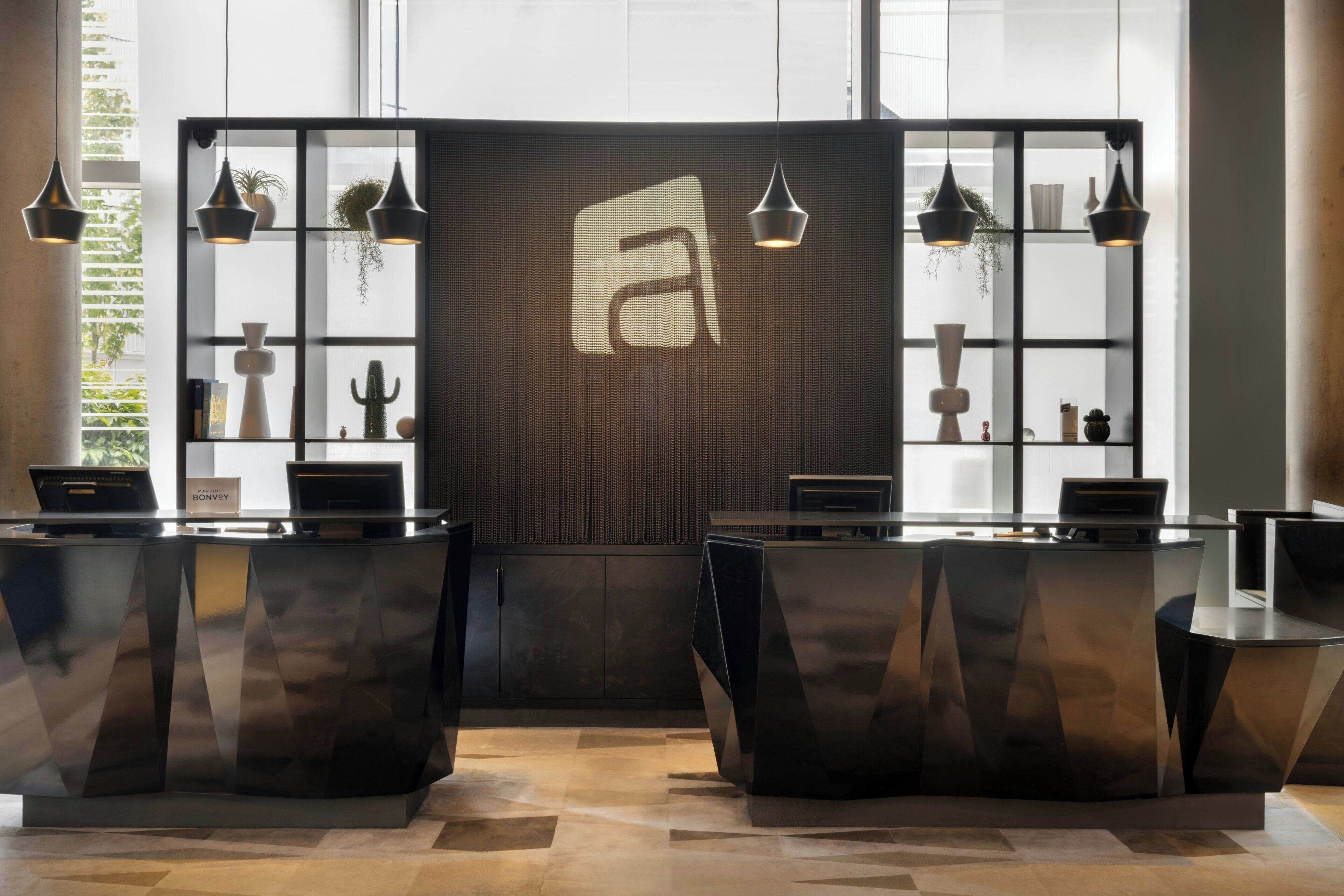 A reception desk area with a modern design, featuring two reception counters, a large window with a view, and a decorative wall with a geometric pattern.