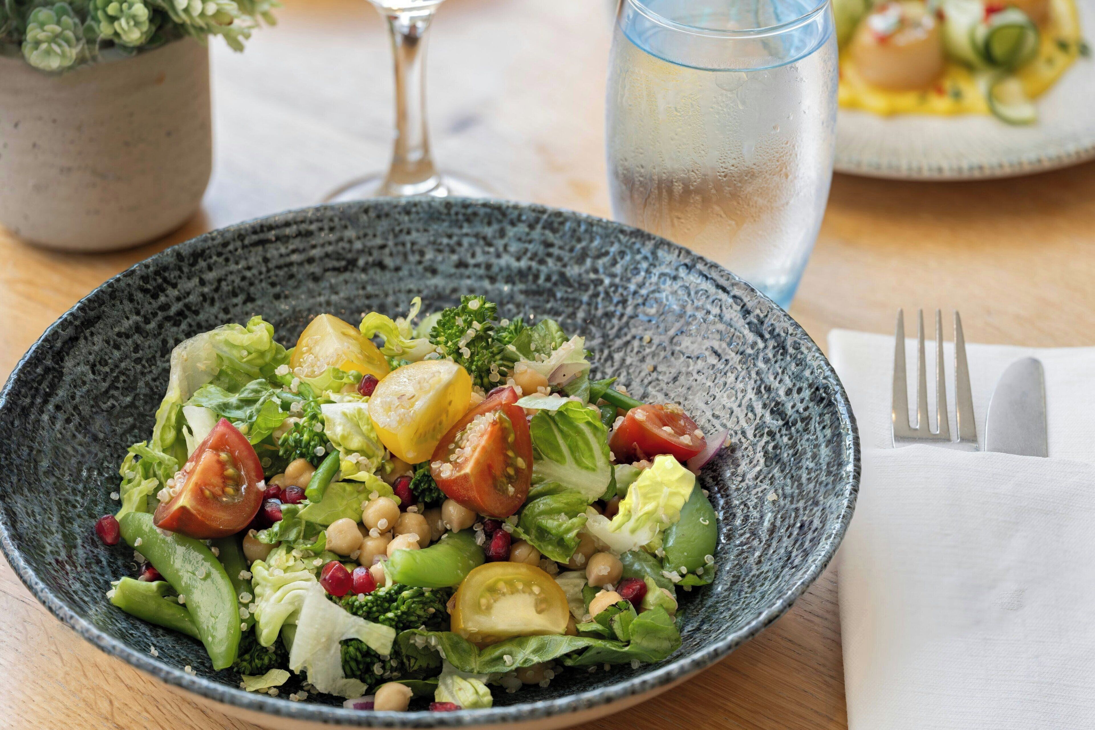Un saladier rempli de salade, avec divers légumes et des pois chiches, posé sur une table.