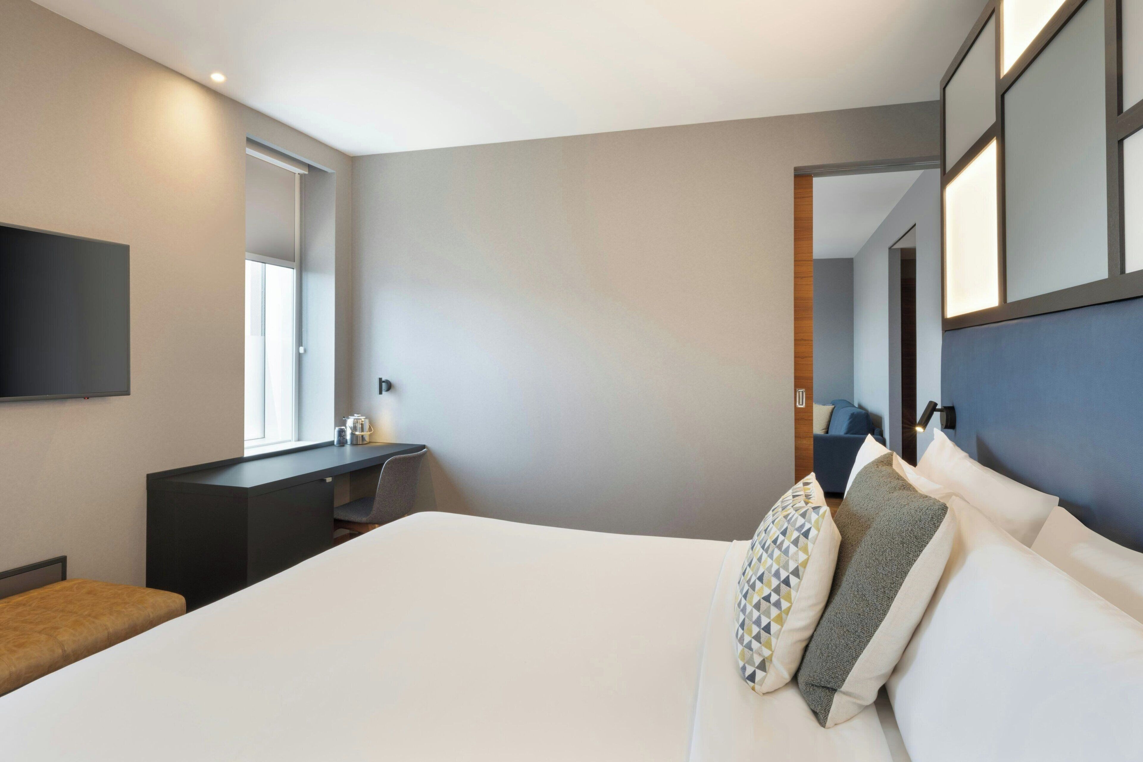 Ein modernes Hotelzimmer mit einem großen Bett, einem Schreibtisch, einem Flachbildfernseher und Blick auf den Flur.