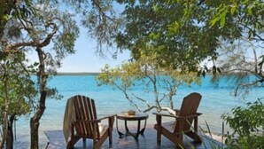 Une terrasse en bois avec deux chaises et une table, donnant sur une étendue d’eau d’un bleu limpide.