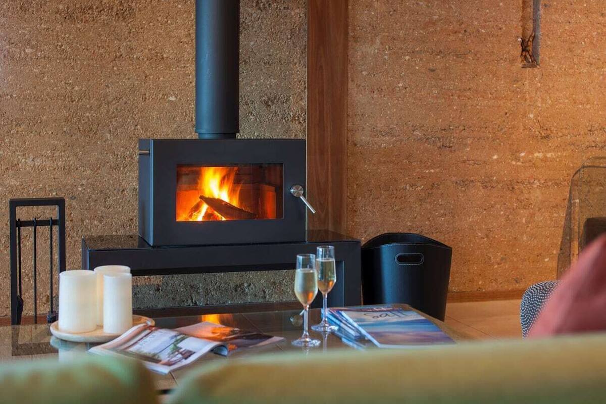 Un cuarto acogedor con una estufa de leña, velas y una mesa de vidrio con revistas y vasos.
