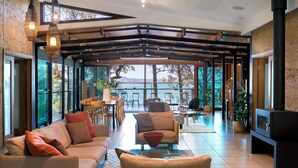 Un vaste espace de vie avec une grande fenêtre donnant sur un plan d’eau, un coin salon confortable et une cheminée.