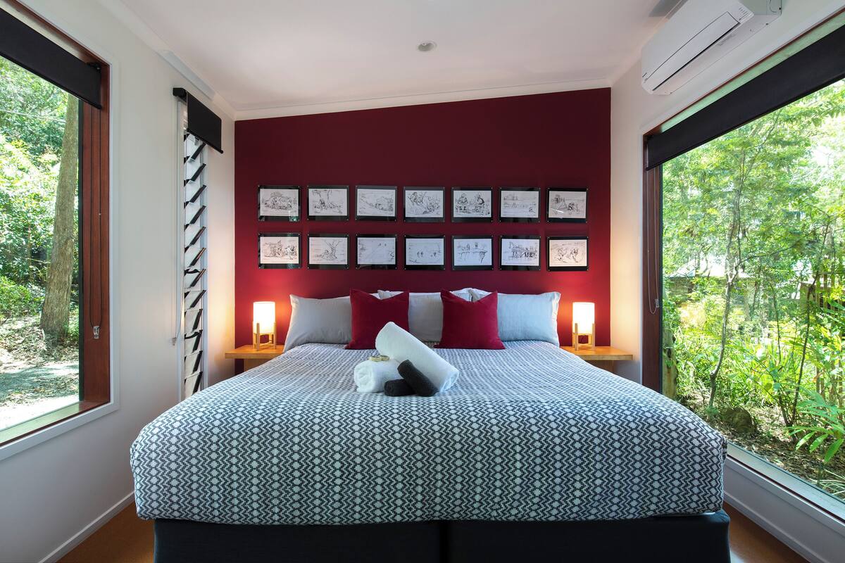Un dormitorio con una colcha estampada, una pared de acento roja y obras de arte enmarcadas sobre la cama.