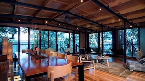 Une pièce spacieuse avec une grande table à manger en bois, des sièges confortables et de grandes fenêtres donnant sur l’extérieur.