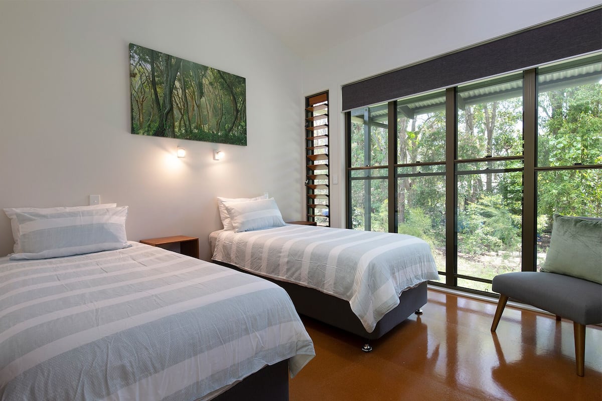 Un dormitorio con dos camas, un ventanal con vistas a árboles y un cuadro en la pared.