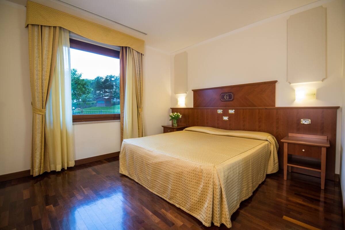A hotel room with a wooden bed, a nightstand, a lamp, and a window with curtains.