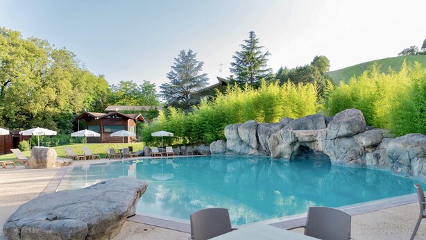 Un área de piscina con una formación rocosa, sillones de descanso y una mesa.