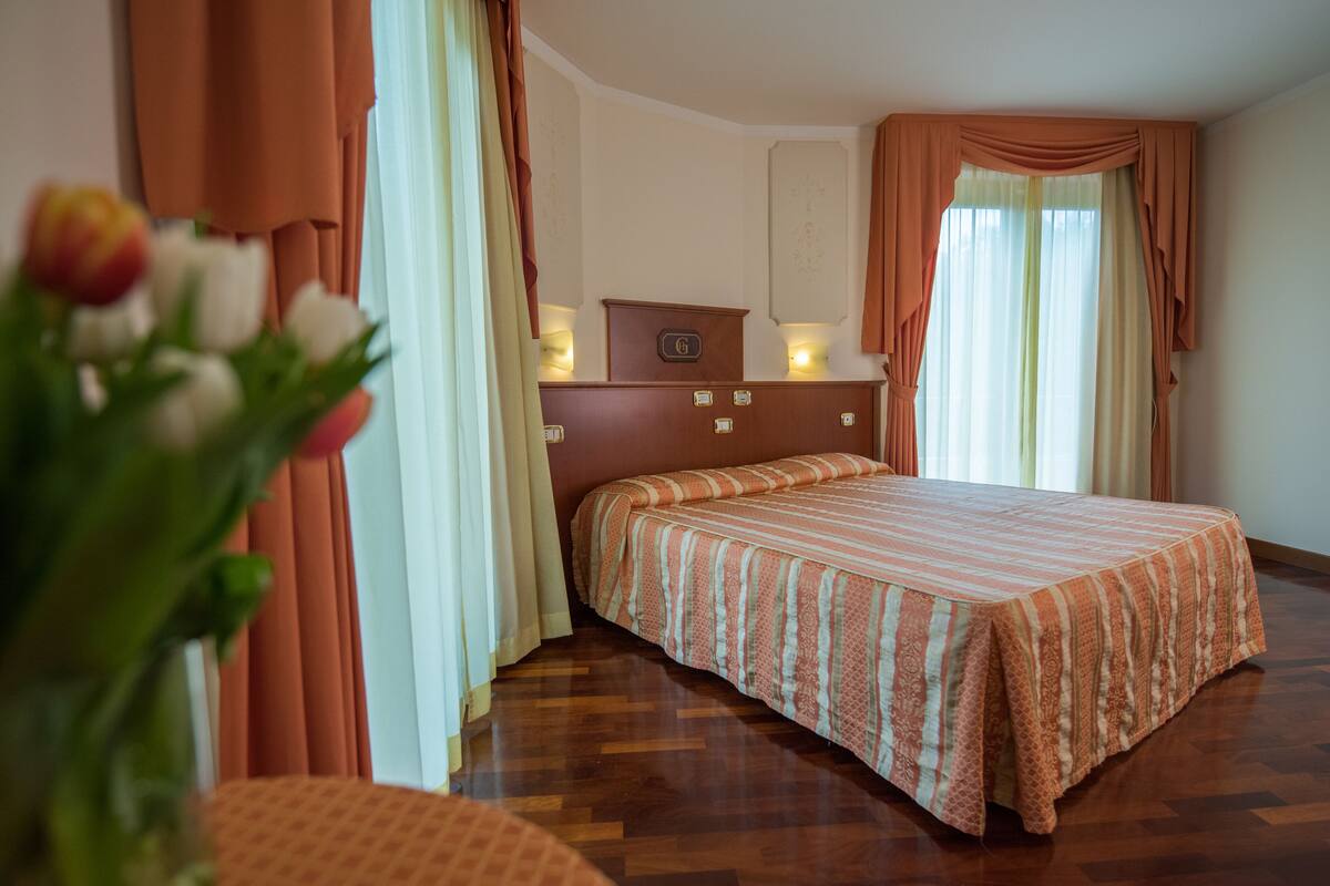 A hotel room with a bed, curtains, a nightstand, and a wall-mounted clock.