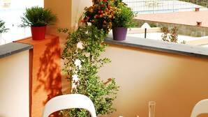 Un balcón con una mesa lista para el desayuno, plantas en macetas y vistas a la costa.