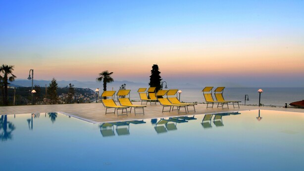 Una piscina con sillas reclinables amarillas y vistas al mar al atardecer.