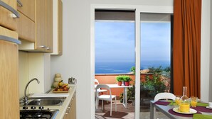 Una cocina con pileta, estufa y alacenas, que da a un balcón con mesa, sillas y vista al océano.