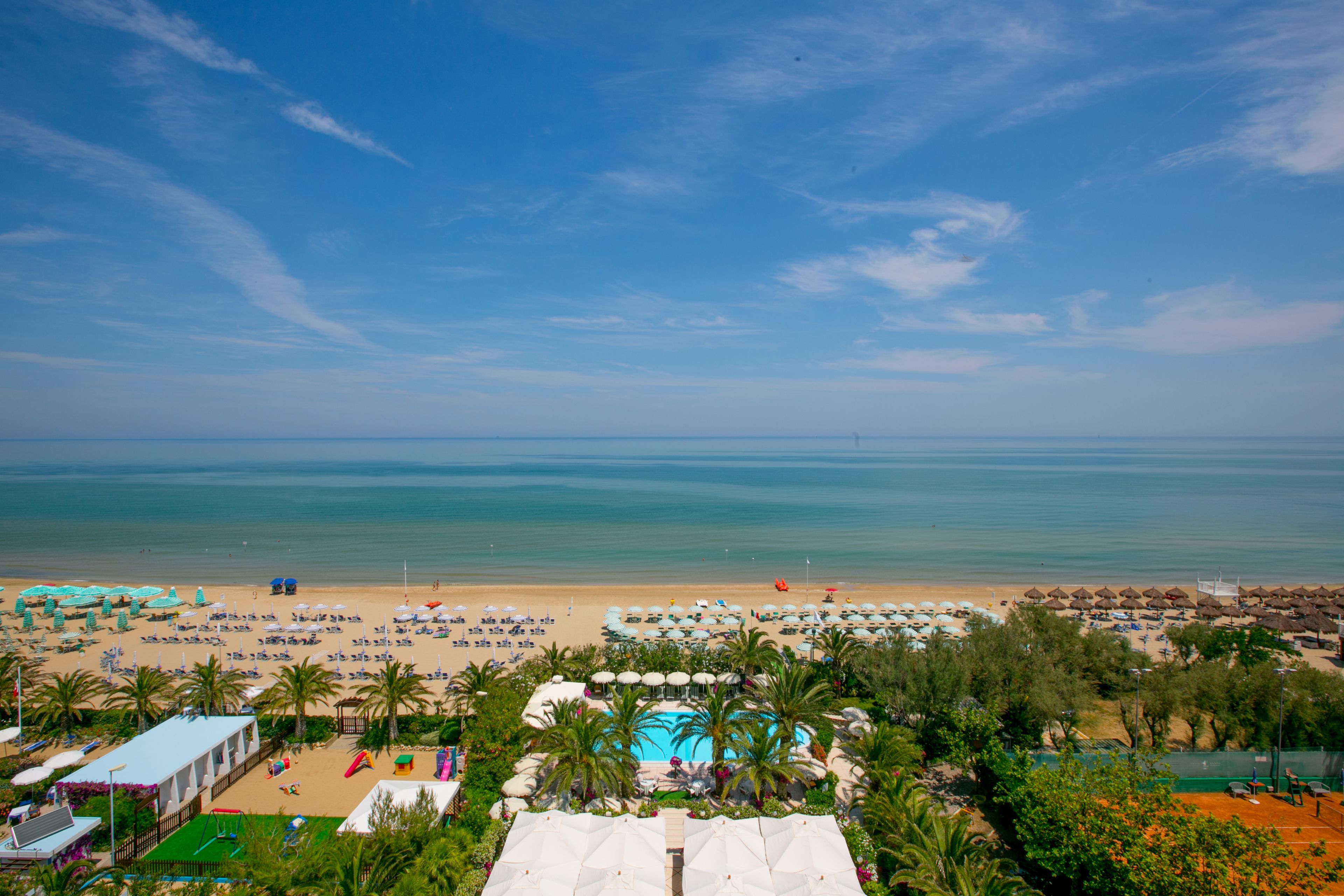 Un complejo turístico en la playa con piscina, sombrillas y sillas.