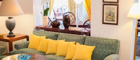 A green sofa with yellow cushions, a small table with a blue object, a lamp, and a vase with flowers.