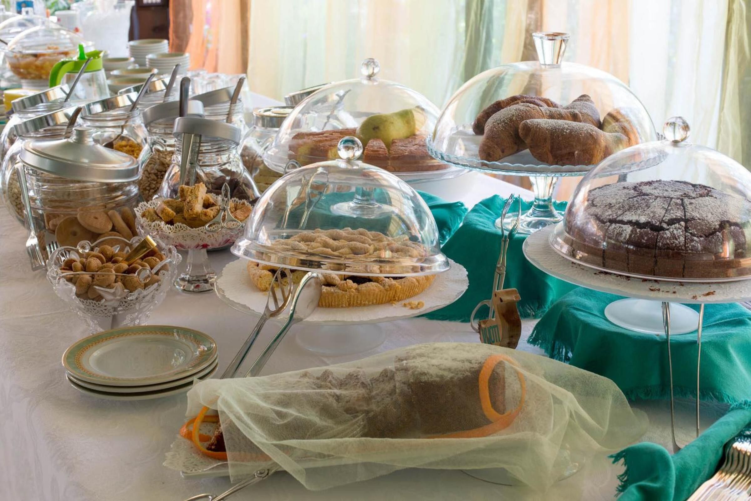 A buffet table with various food items covered with glass domes, including pastries, cookies, and a cake.