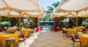 An outdoor dining area with yellow tables and chairs, white umbrellas, and a pool in the background. - LH Mion Hotel (Silvi)