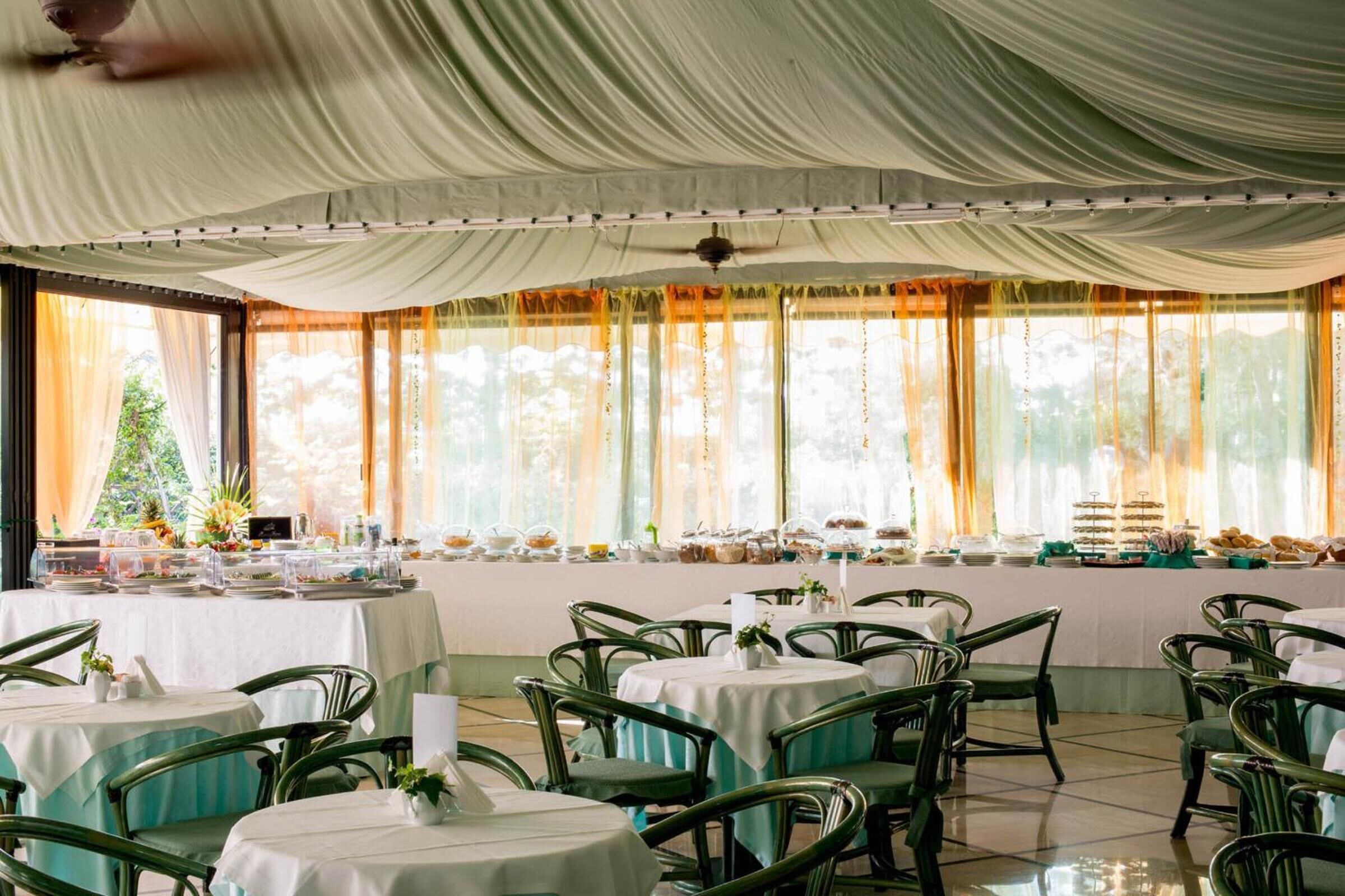 A banquet hall with round tables, green chairs, and a buffet setup.