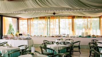 A banquet hall with round tables, green chairs, and a buffet setup.