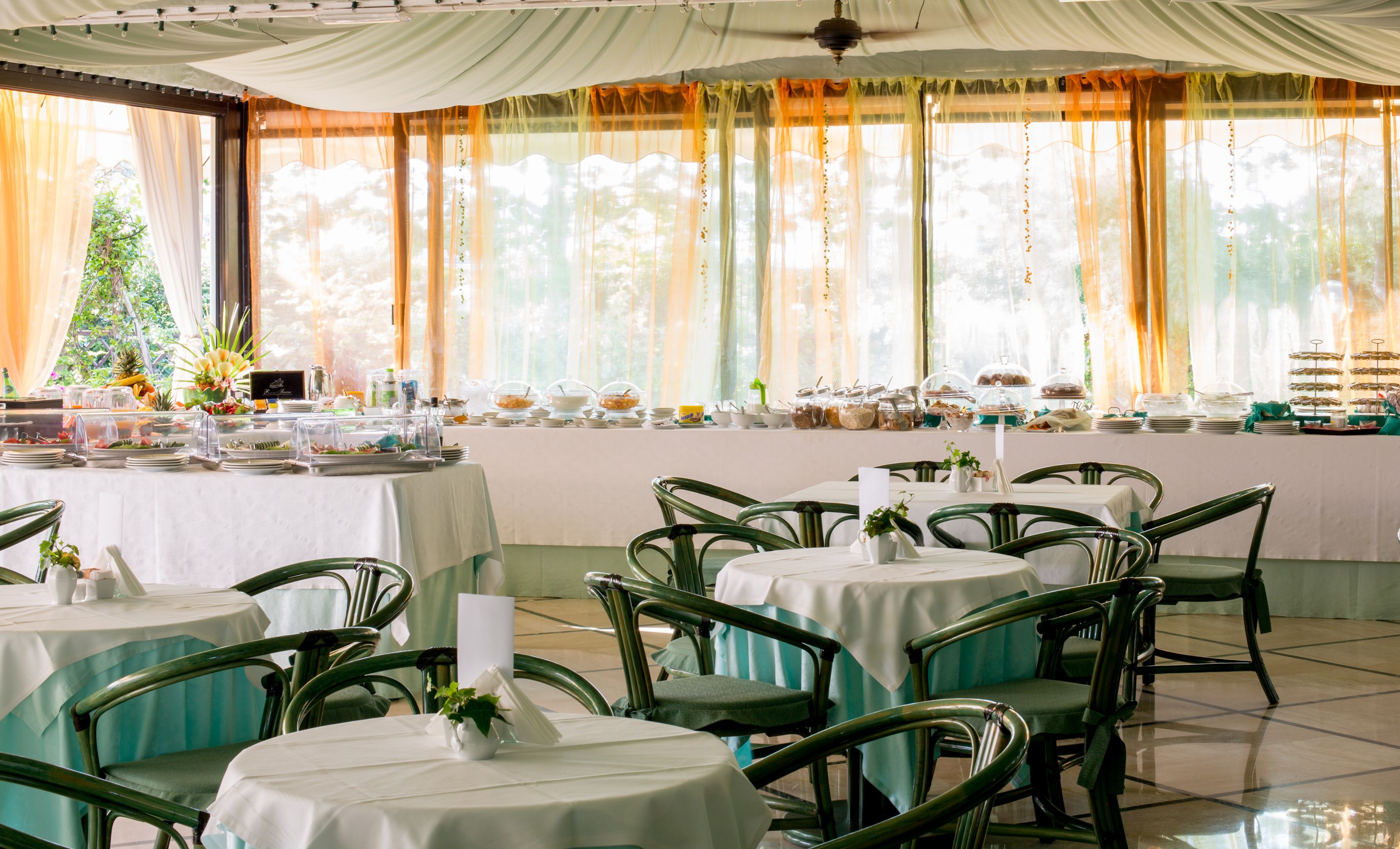 A dining area with round tables, green chairs, and a buffet with various food items.
