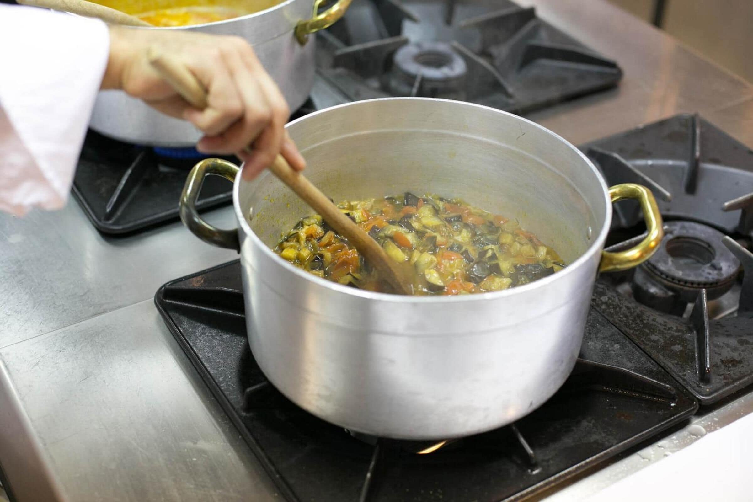 A stainless steel pot on a gas stove with a wooden spoon stirring a stew.