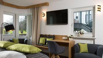 A modern hotel room with a bed, a desk with a chair, a TV, and a window with a view of a staircase.