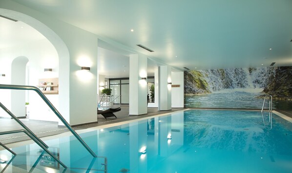 An indoor swimming pool with a waterfall mural, clear glass walls, and a modern design.