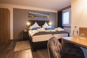 Una habitación de hotel con cama, escritorio, silla, mesita de noche, ventana y un cuadro en la pared.