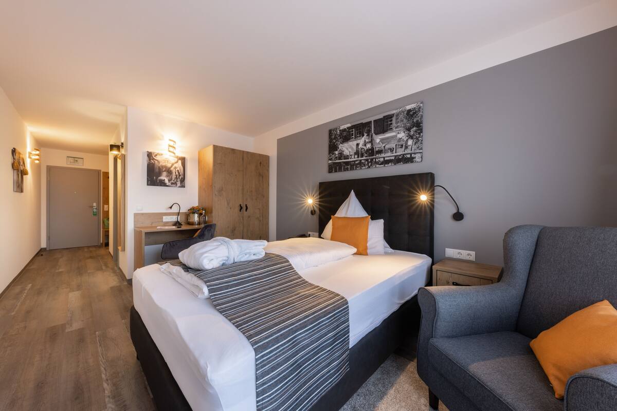 Une chambre d’hôtel moderne avec un grand lit, un bureau et un fauteuil gris.
