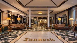 A spacious lobby with a checkered floor, leather seating, and a central column. - Hotel Tanneck (Bad Woerishofen)