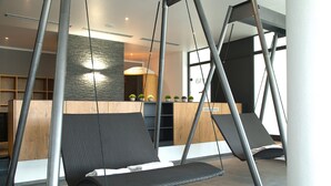 A modern interior with a reception desk, a stone wall, and two swing chairs. - Hotel Tanneck (Bad Woerishofen)