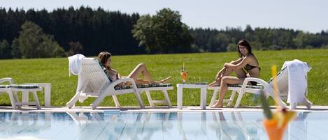 A poolside area with lounge chairs and a clear view of a grassy field in the background.