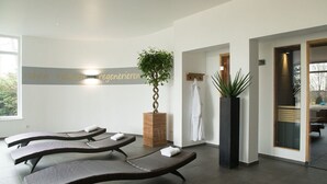 A spa room with three loungers, a large potted plant, and a wall with a sign. - Hotel Tanneck (Bad Woerishofen)