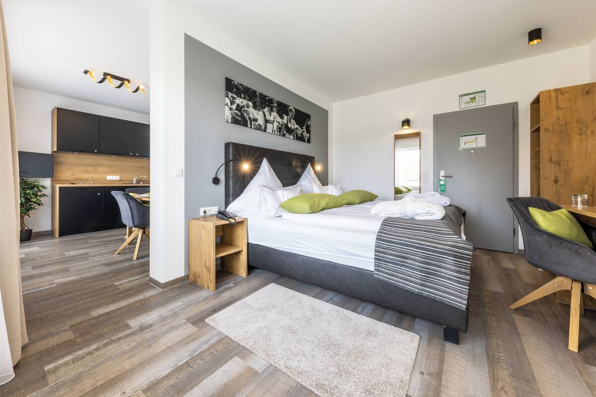 Une chambre moderne avec un grand lit, un bureau et, au fond, un coin cuisine.