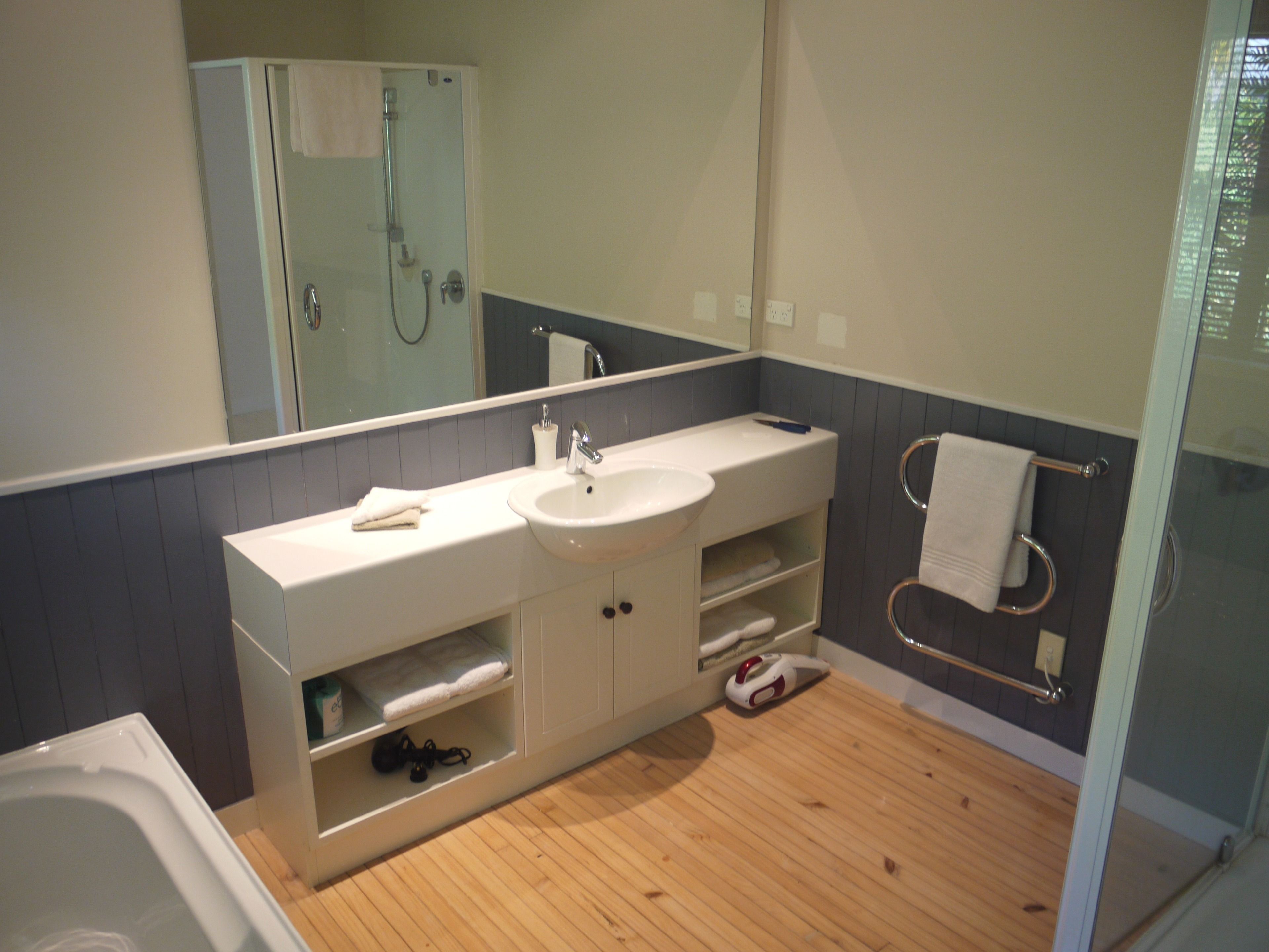 A modern bathroom with a wooden floor, a white sink, a mirror, and a glass shower enclosure.