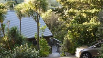 A house with a sloped metal roof, surrounded by lush greenery and palm trees.