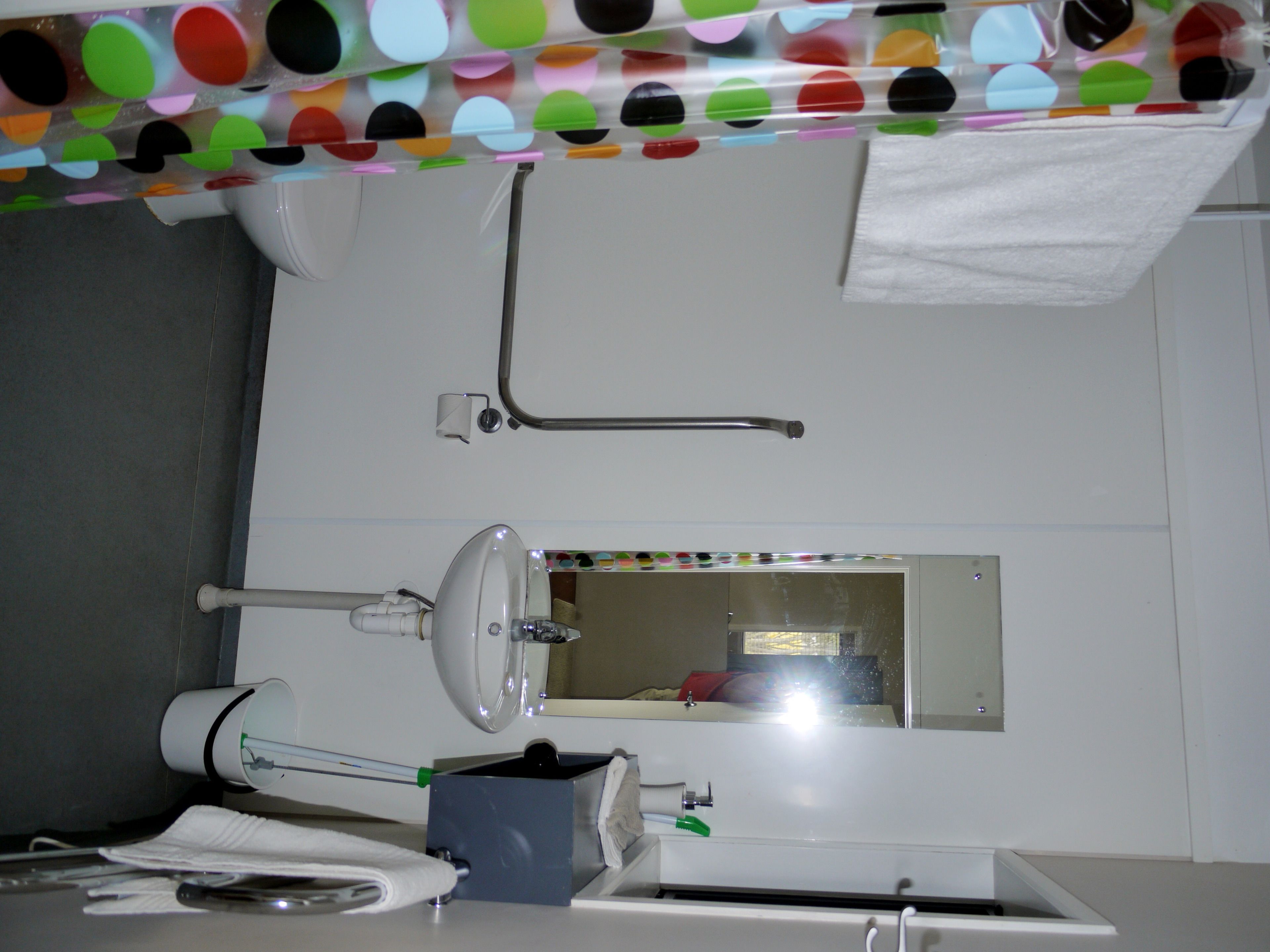 A bathroom with a toilet, sink, mirror, towel rack, and a towel dispenser.