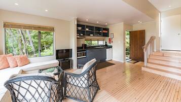 A modern kitchen with built-in appliances, a dining area with wicker furniture, and a view of the forest through large windows.