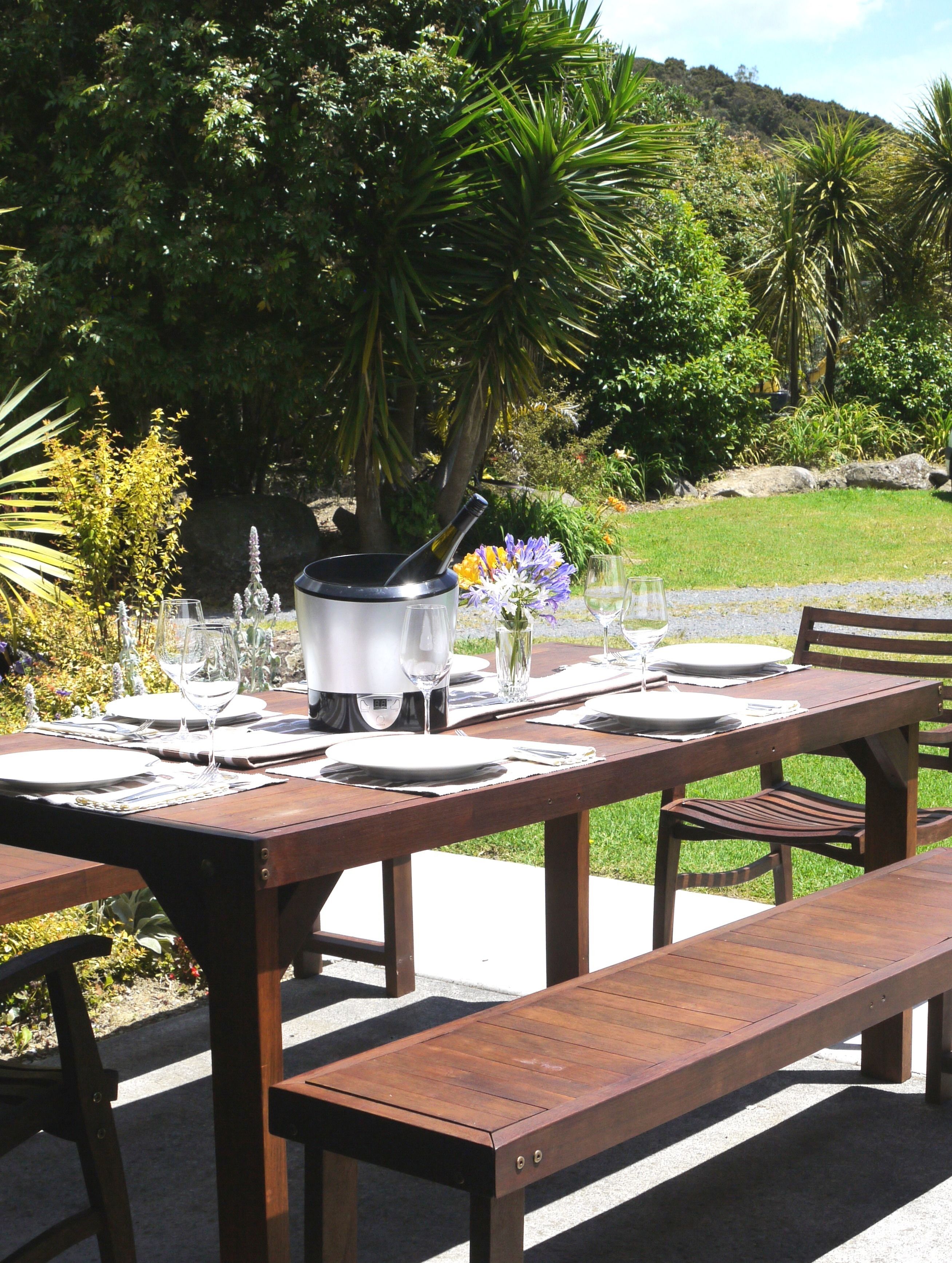 Un espacio para comer al aire libre con una mesa de madera preparada para una comida, una parrilla y un banco.