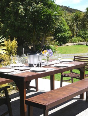Een eethoek buiten met een houten tafel gedekt voor een maaltijd, een barbecue en een bank.
