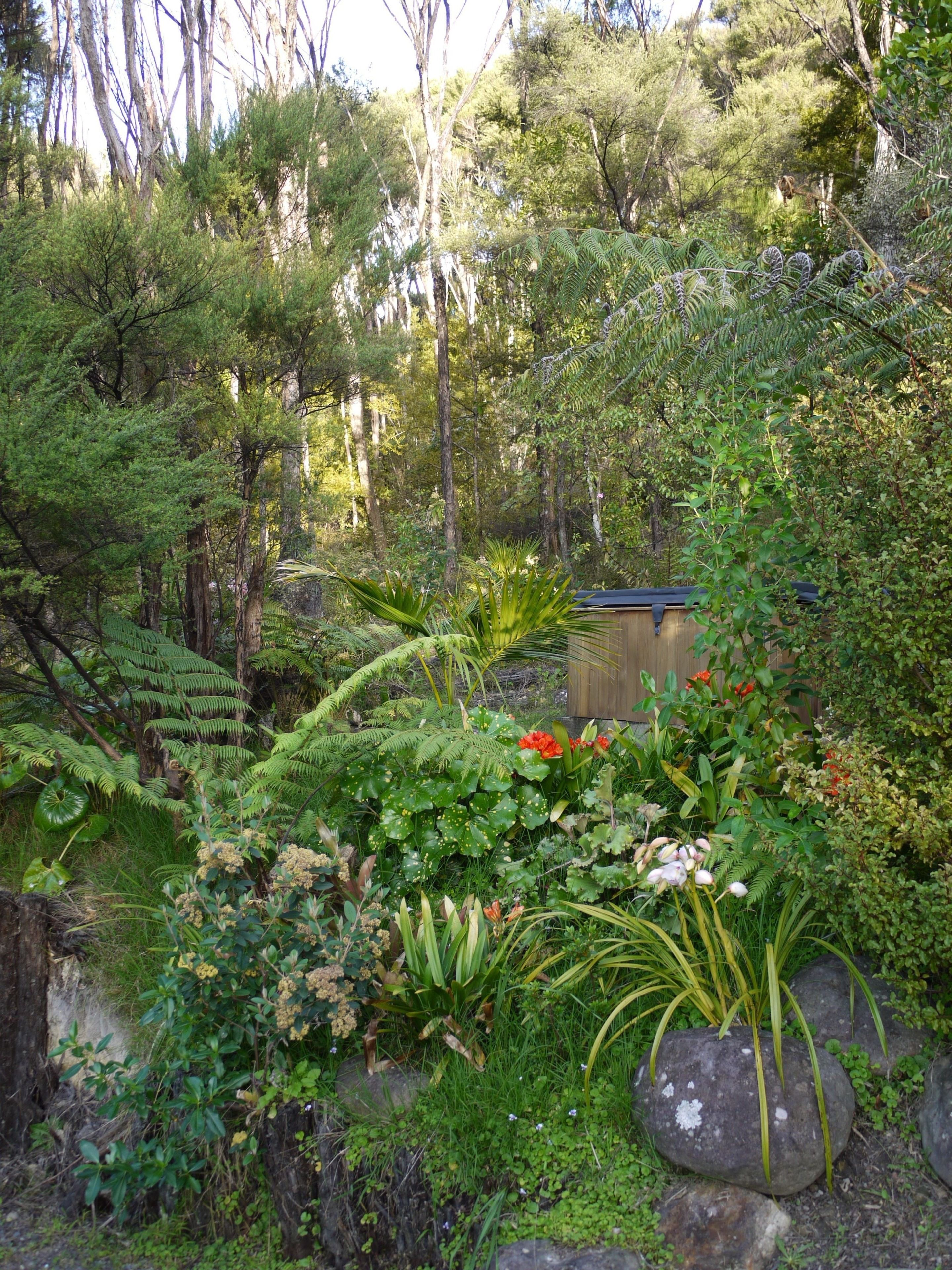 A lush garden with various plants, a wooden structure, and a stone wall.