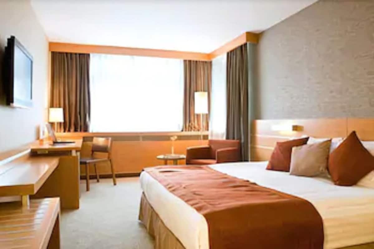 A hotel room with a bed, a desk, a chair, a small table, and a TV.