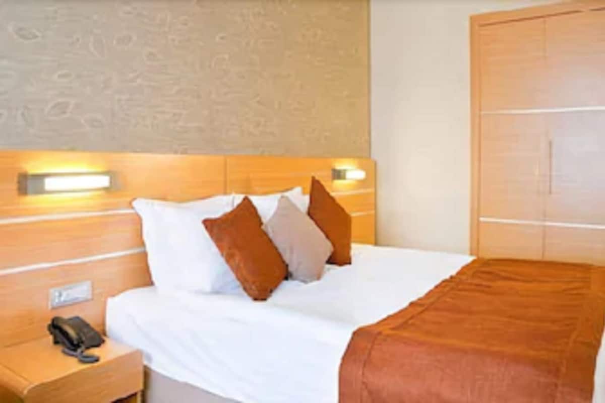 A hotel room with a wooden headboard, a bed with white linens and brown pillows, a bedside table with a phone, and a wardrobe.