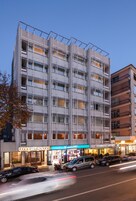Un hotel de varios pisos con fachada moderna, con balcones y un espacio comercial en la planta baja que alberga una Starbucks Coffee.