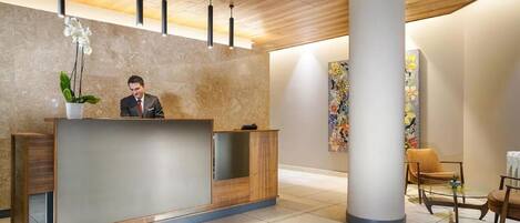 A reception area with a wooden reception desk, a large pillar, and a seating area with chairs and a table.