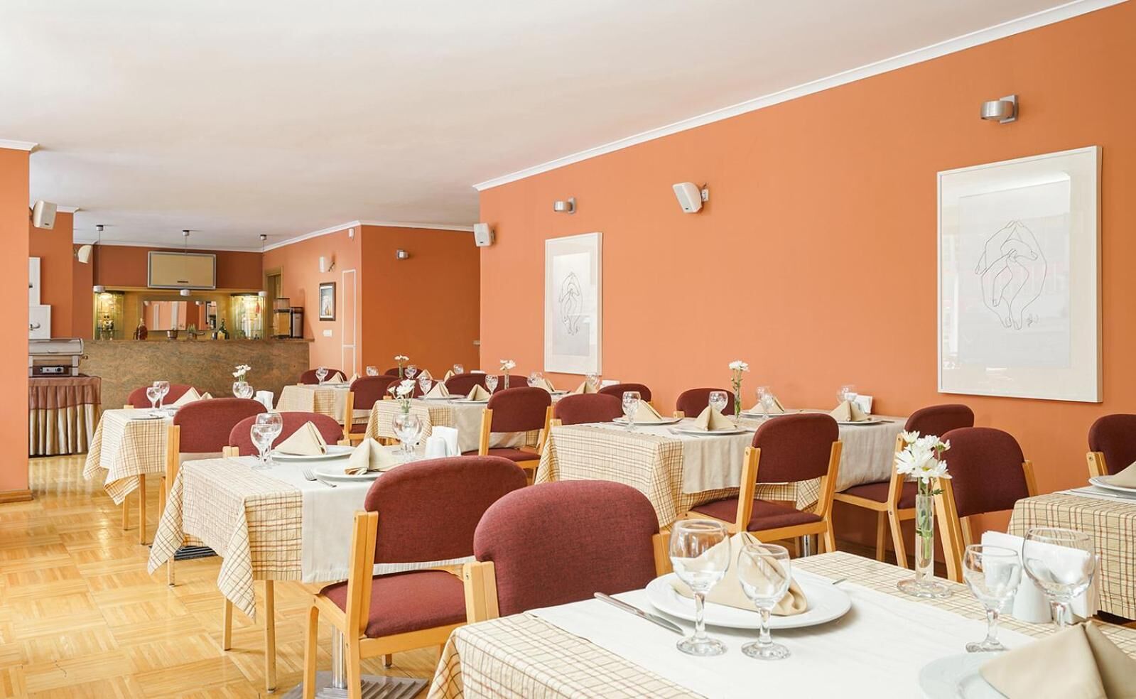 Un restaurante con varias mesas y sillas, una zona de cocina al fondo y obras de arte en las paredes.