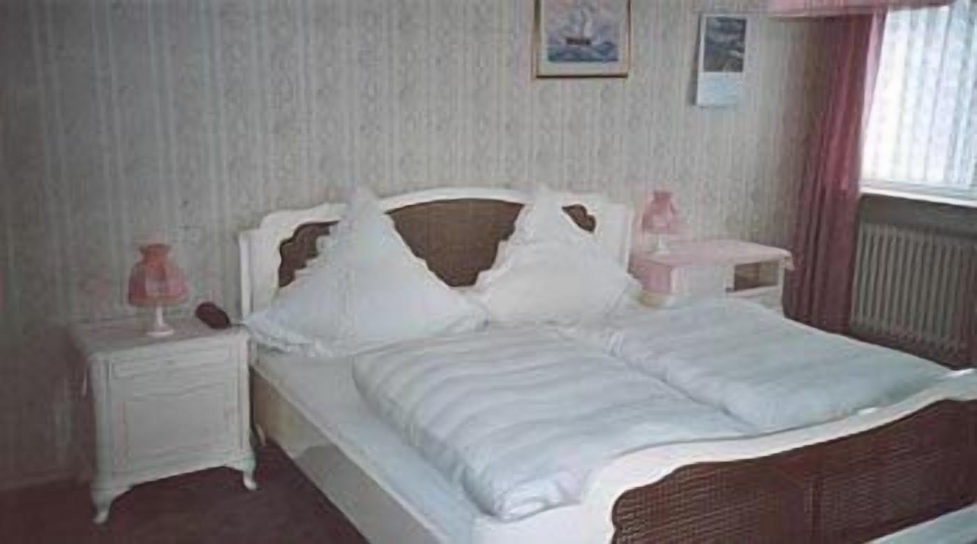 Un dormitorio con una cama blanca, una mesita de noche y una ventana con cortinas.