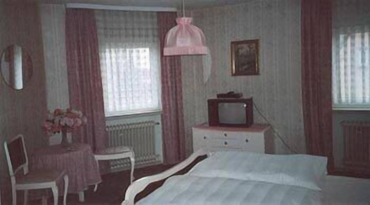 A bedroom with a bed, a television on a dresser, a chair, and a table with flowers.