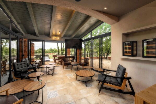 An indoor patio area with round tables and chairs, large windows, and a brick fireplace.