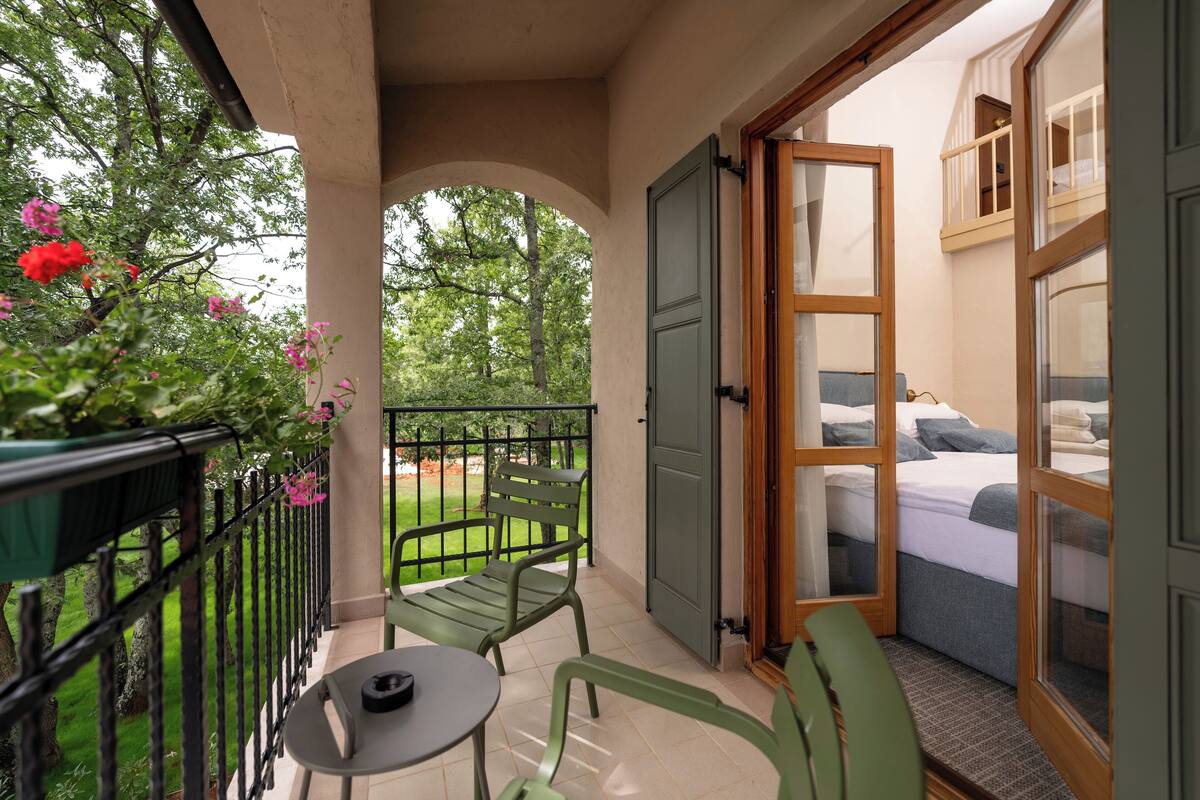 Ein Balkon mit Tisch und Stühlen, ein Bett mit Blick und ein grünes Geländer.