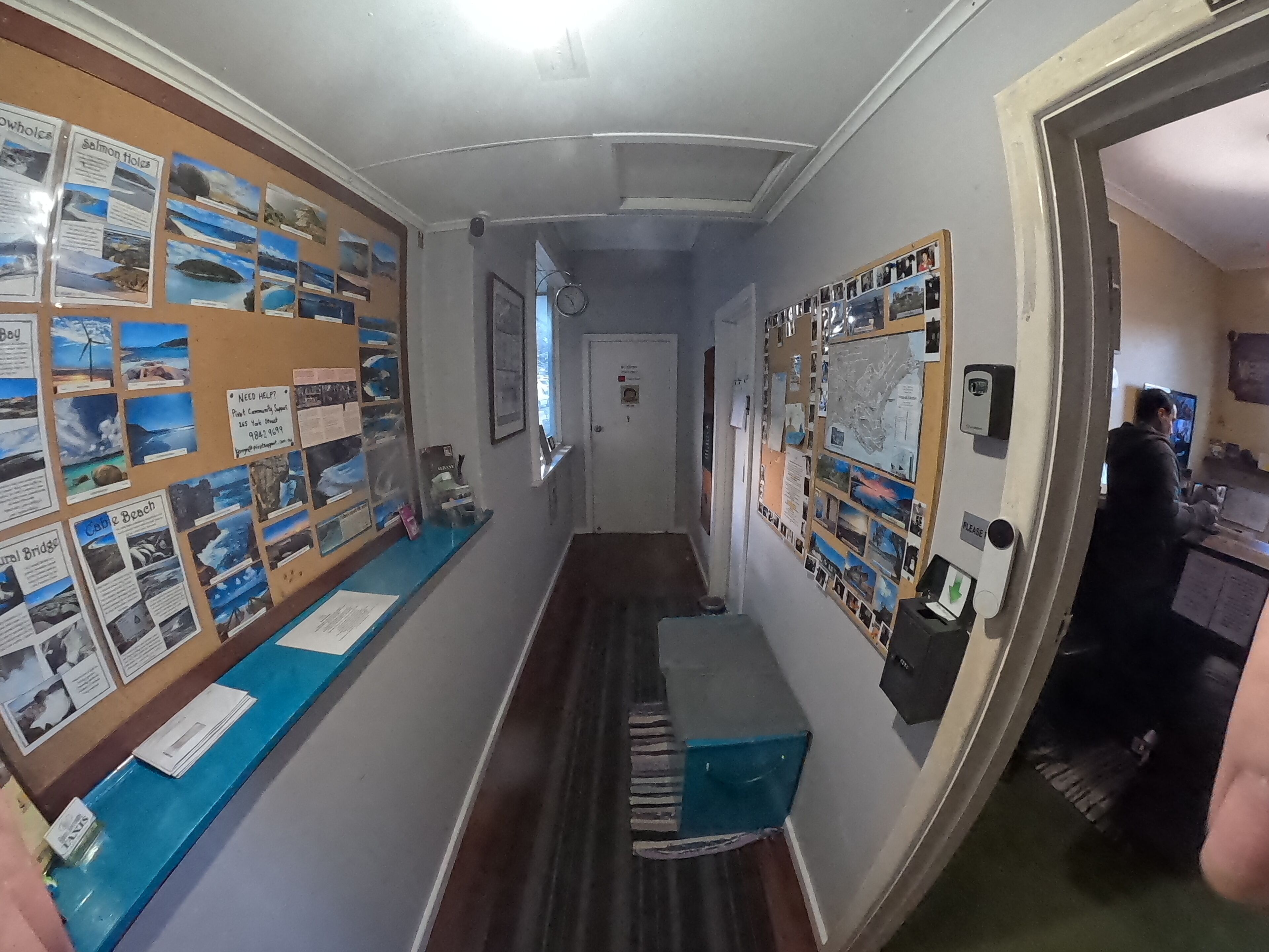 A hallway with informational displays on both sides, a clock on the wall, and a counter with a blue surface.