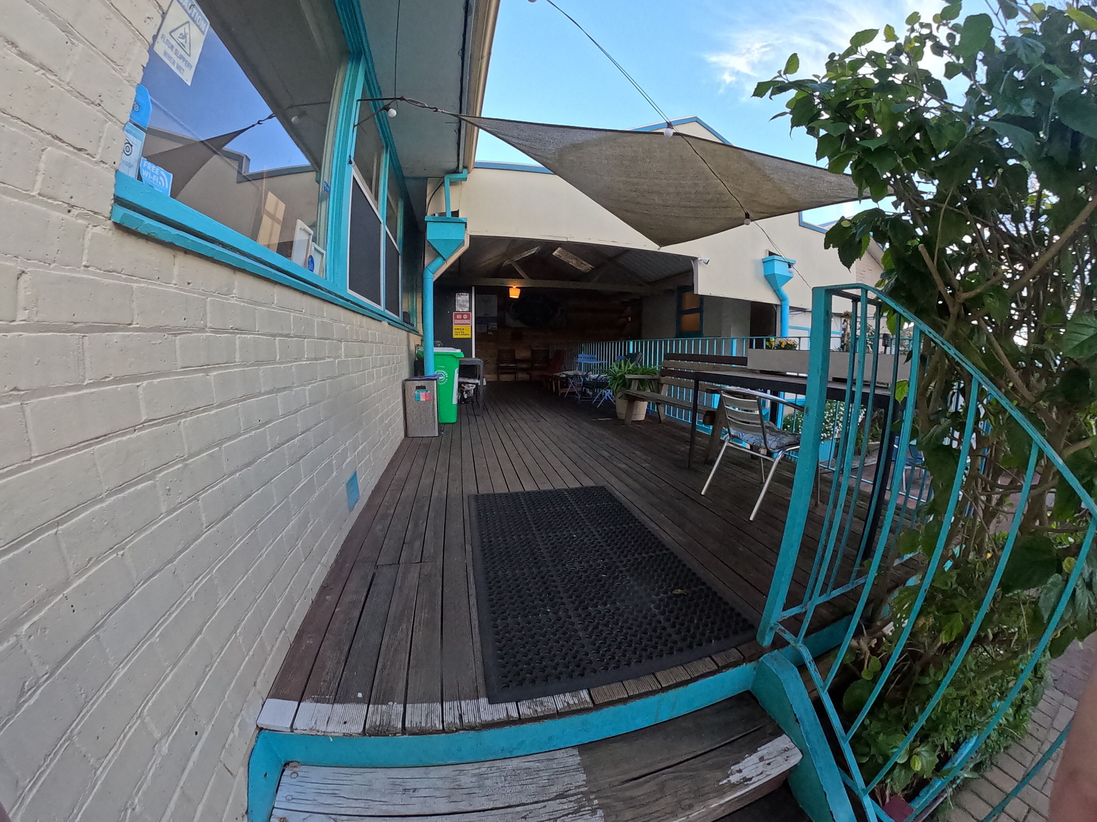 A wooden deck with outdoor seating, a trash bin, and a covered area with a bench.